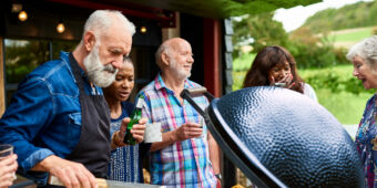An older man is grilling vegetables at garden party with his family