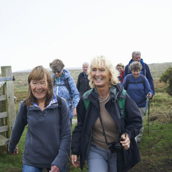 A group of smiling, middle-aged women and men hiking through farmland