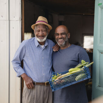 A senior man in his allotment showing off his home grown vegetables with his son